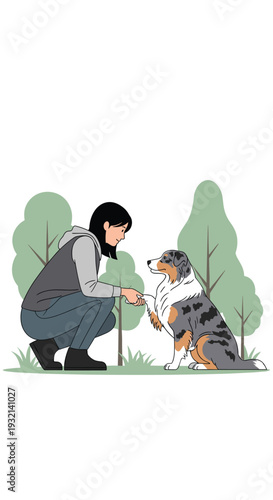 A woman in a grey hoodie crouches to shake hands with a tri-color Australian Shepherd dog in a grassy outdoor setting.