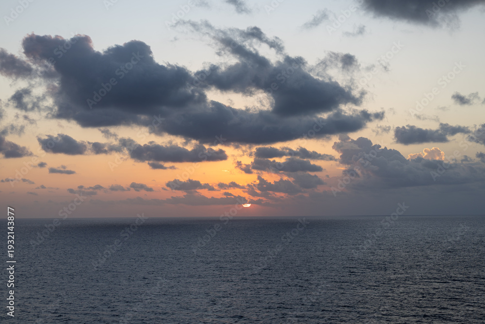 Obraz premium Soft Caribbean Sunrise with Orange Horizon and Scattered Clouds Over the Ocean