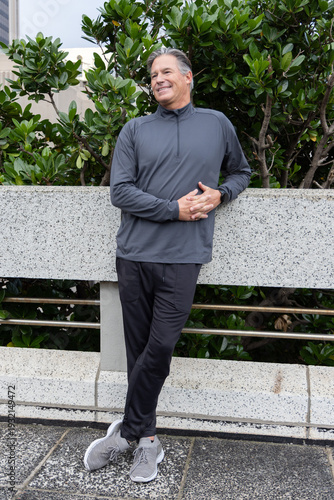 Fotografie Middle-aged man standing and leaning against speckled planter wall on urban plaz