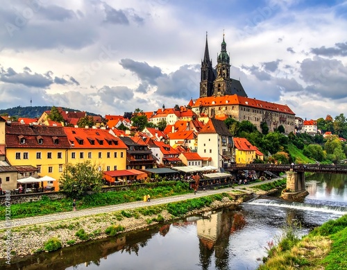 Picturesque medieval town with red-tiled roofs, a river, a bridge, and a castle with spires
