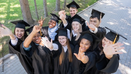 Students of different nationalities in graduation gowns wave their hands. 