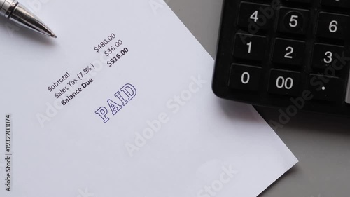 Close up of paid stamp being pressed onto invoice with calculator and pen nearby