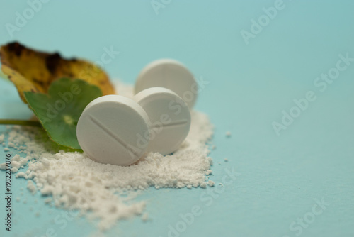 Minimal healthcare concept with pills and green leaves on blue background