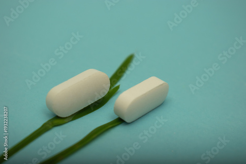 Minimal healthcare concept with pills and green leaves on blue background