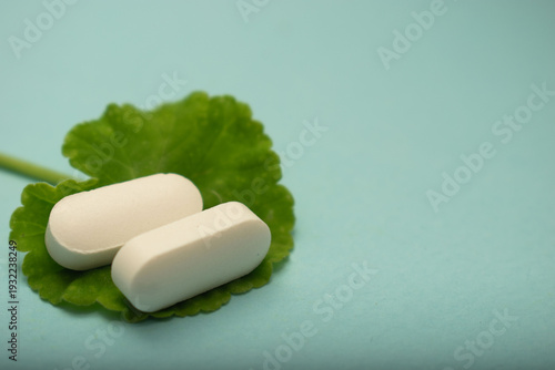 Minimal healthcare concept with pills and green leaves on blue background