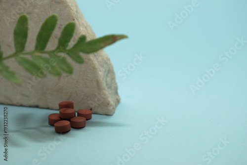 Minimal healthcare concept with pills and green leaves on blue background