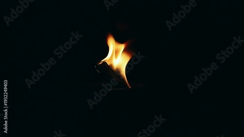 Close up of a bright fire flame burning on a wooden torch or bonfire in pitch black darkness. Concept of light, survival, heat, and energy. Abstract element of wild fire, danger.