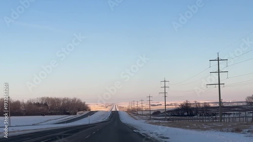 Empty rural prairie road at golden hour with farmland and utility poles