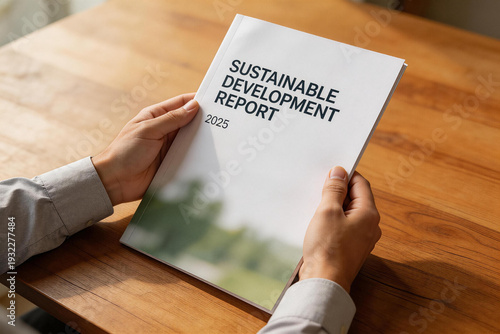 A person holds a sustainable development report booklet on a wooden table.