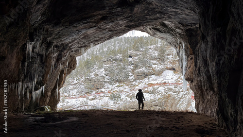 Cuadro en lienzo Wide-mouthed cave structure, curious explorer, and ice stalactites hanging from the ceiling in winter