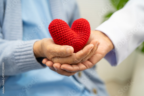 Doctor giving a red heart to senior patient in hospital.