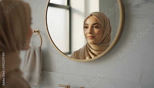 A confident young Muslim woman looking in a bathroom mirror, reflecting on self-care and beauty concept with warm, natural light.