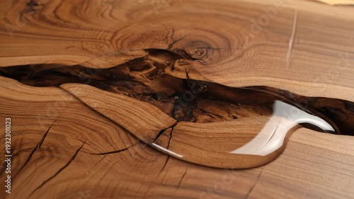 Clear epoxy resin is poured onto a beautiful wooden surface. It fills natural cracks, creating a stunning river table design.