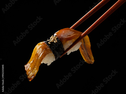 Konstfotografi Close up of chopsticks holding eel nigiri sushi with sweet sauce on black backgr