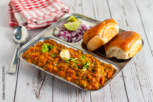 Spicy pav bhaji served with buttered bread rolls, garnished with onions, coriander, lemon, vibrant street food presentation style.
