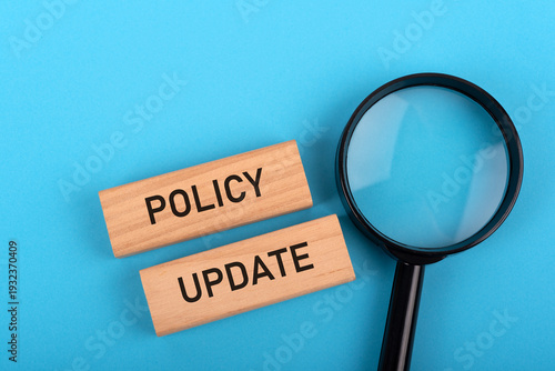 Magnifying glass and policy update text on wood block on blue background