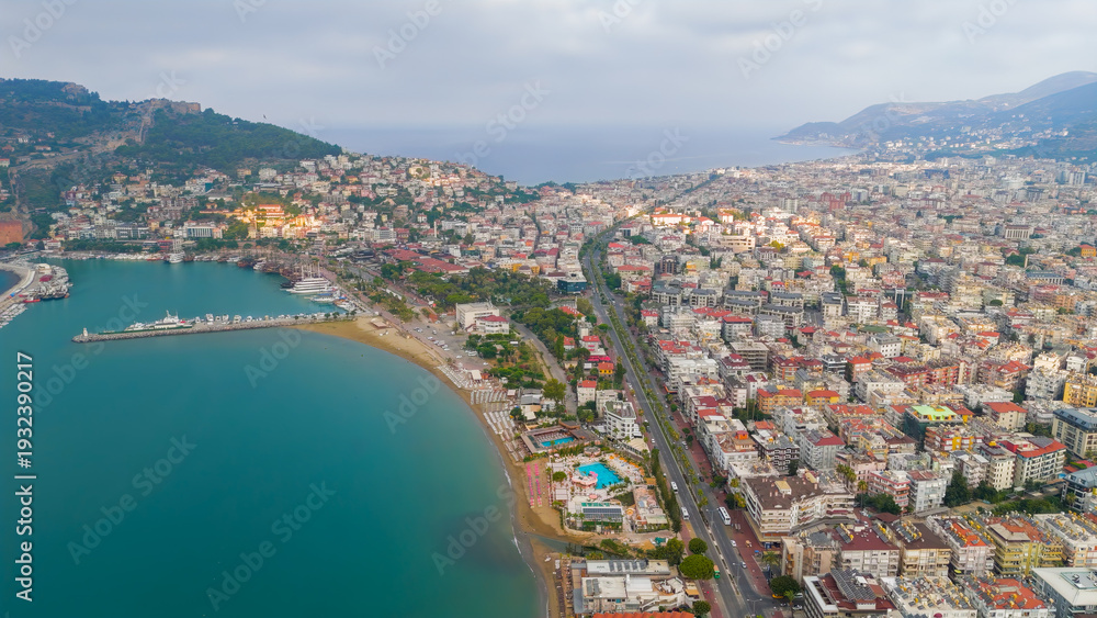 Fototapeta premium Alanya, Turkey. Municipal beach with surf and umbrellas, seafront hotels, marina and coastal road with cars in Alanya summer season.. Aerial View