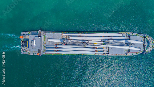 Large heavy lift cargo ship transporting massive wind turbine blades across the deep blue ocean. Global logistics for renewable energy and maritime shipping industry business concept.
