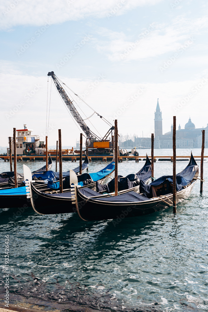 Fototapeta premium Gondolas docked at the waterfront in Venice near construction and towers