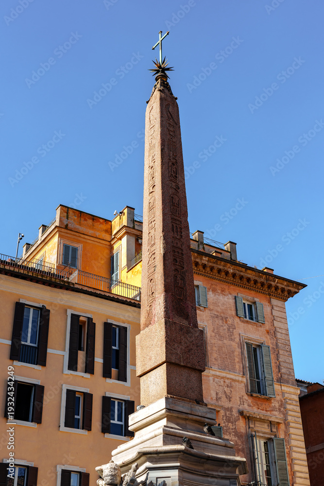 Naklejka premium Tall obelisk stands in the city center near historic buildings under a clear sky