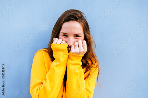 Shy girl covering her mouth with hands and smiling on a blue background