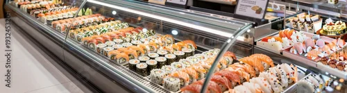 Obraz  z motywem Assorted sushi rolls displayed in glass refrigerated deli case
