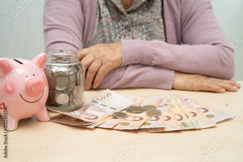 Retired elderly woman counting coins money with piggy bank and worry about monthly expenses and treatment fee payment.