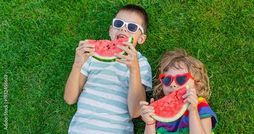 Happy children in sunglasses eating watermelon slices on green grass