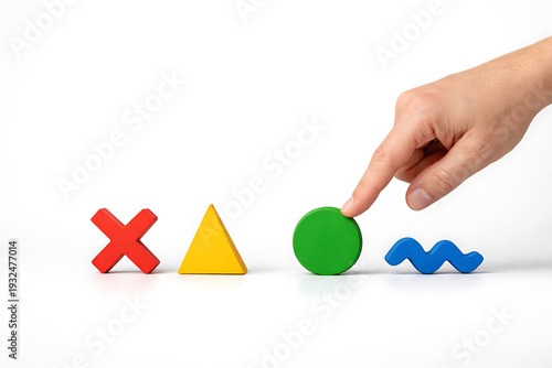 A hand picks up a green circle from a row of colorful shapes on a table.