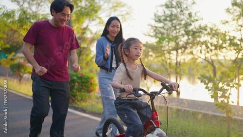 Asian young girl riding bicycle in garden while her parents look after. 