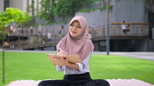 Asian young Muslim woman taking notes in her diary journal in the city. 