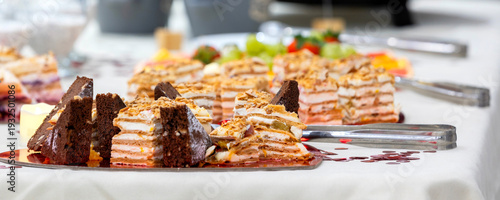 Assorted layered cakes and pastries on festive dessert table with fresh fruit, banner