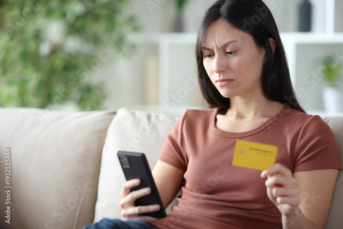 Annoyed asian woman paying online with credit card and phone