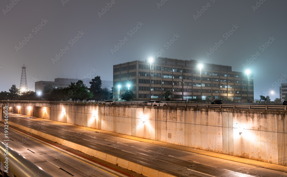 Fototapeta premium Scenic night view of an illuminated state government office building and an empty multi-lane highway underpass surrounded by dense fog in Oklahoma City, United States