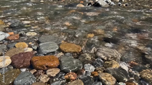 Flowing water gently cascades over smooth pebbles and stones along a riverbank, showcasing the natural beauty of a serene aquatic environment