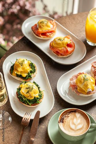Foto A gourmet brunch spread featuring various poached egg dishes including Eggs Royale with salmon, Eggs Florentine with spinach, and classic Benedict with ham, served with a cappuccino