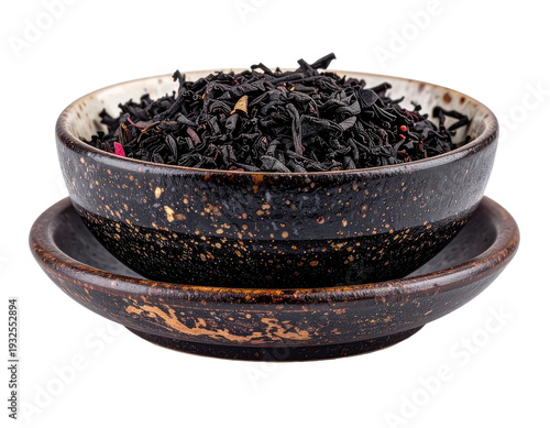 A decorative dark bowl holds a pile of dried black tea leaves