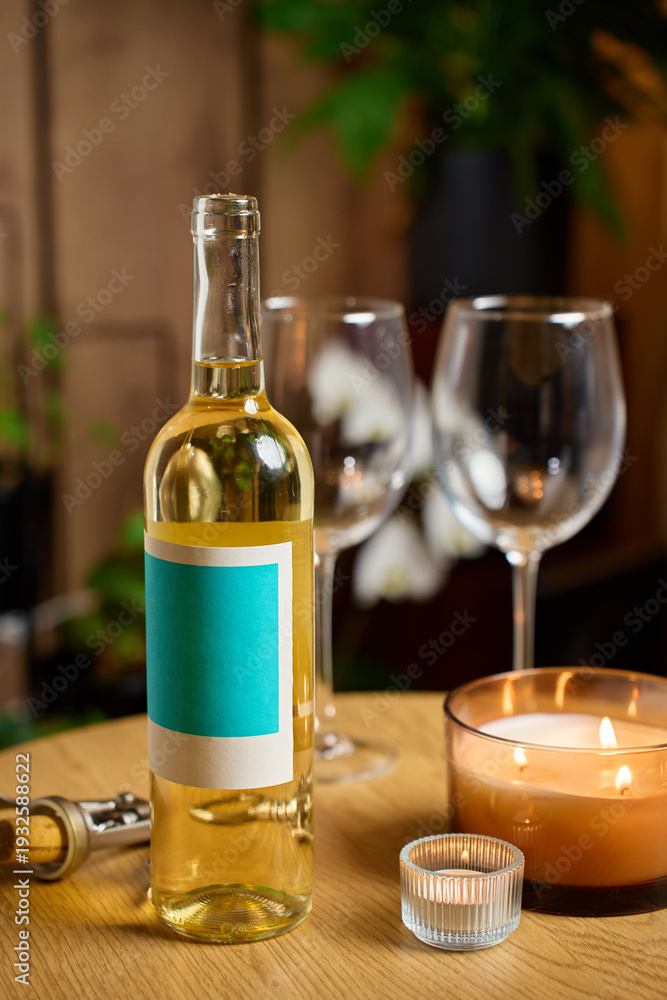 Obraz premium Bottle of white wine, two empty wine glasses and burning candles on table in cozy home interior. Concept of romantic dinner, date night and drinking wine