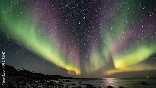 Northern lights illuminate night sky over rocky shoreline with vibrant green and purple auroras dancing above calm ocean waters reflecting starlight