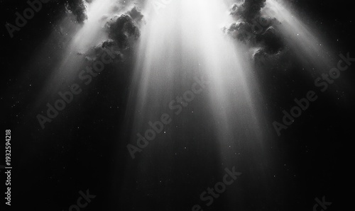 dramatic monochrome sky with clouds and radiant beams of light piercing darkness, scattering fine particles and evoking awe and mystery