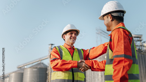 Fotografía Two engineers wearing safety helmets shake hands, proposing a collaboration agreement for a project to construct a factory