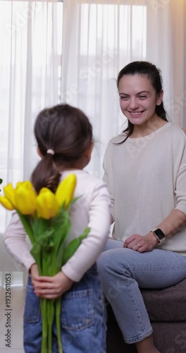 Cute little girl giving her happy mother a bouquet of yellow tulips and then hugging her tightly