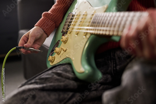 Tablou pe pânză Caucasian teenager plugging electric guitar cable into instrument, sitting indoo
