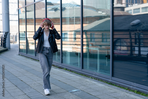 Foto Young woman walks with headphones near glass building in city during daytime