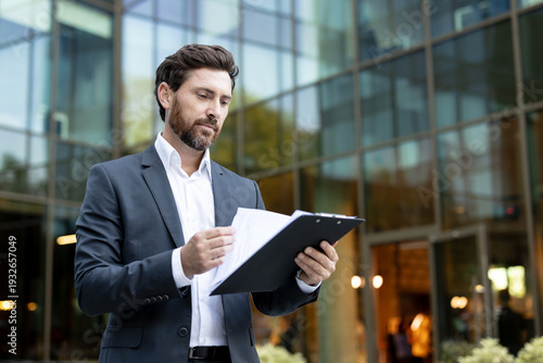 Valokuva Young professional businessman in a sleek suit carefully reviewing reports and d