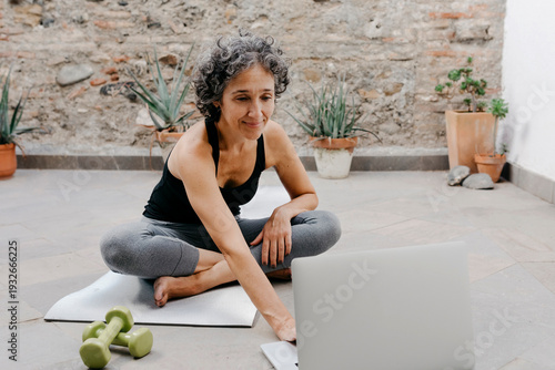 Smiling woman using laptop for learning yoga through online tutorial while sitting at back yard