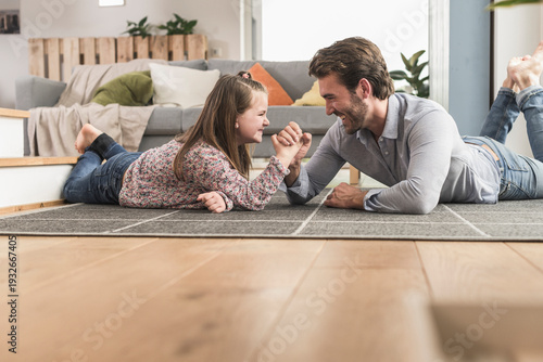 Young man and little girl lying on ground, arm wrestling