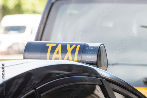 Close-up of a modern black taxi sign with yellow text on a car roof. Urban transportation, city taxi service and public transit in daylight.