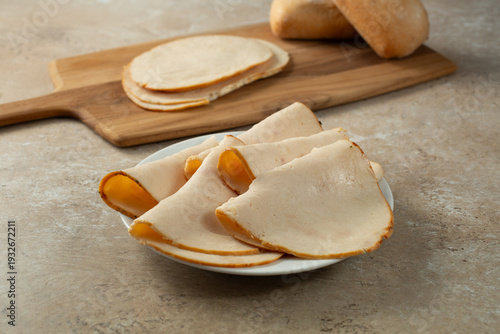 A view of a folded slices of oven roasted chicken breast deli meat, on a plate.