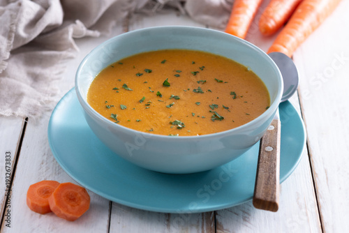 Creamy carrot soup in blue bowl on white wooden table